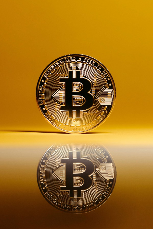 Gold Bitcoin coin standing upright with its reflection on a glossy golden surface