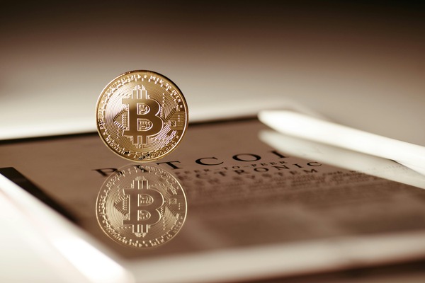Gold Bitcoin coin reflected on a surface printed with the Bitcoin whitepaper text